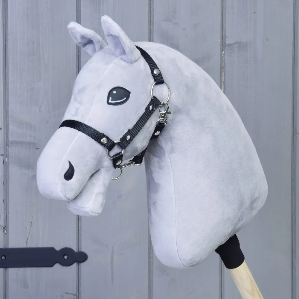 The Build your horse by related_to_12441055625556 is a handmade hobby horse with a plush gray head, black halter, and wooden stick, shown against gray wooden paneling.