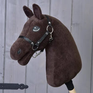The Build your horse plush hobby horse, by related_to_12441055625556, features a dark brown head, brown-chestnut manes, black bridle and reins, and is mounted on a wooden stick against a gray wooden background.