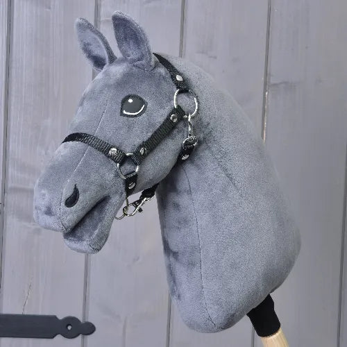The "Build your horse" by related_to_12441055625556 features a plush dark grey head, light grey yarn mane, black bridle and reins, and is mounted on a wooden stick in front of gray wooden panels.