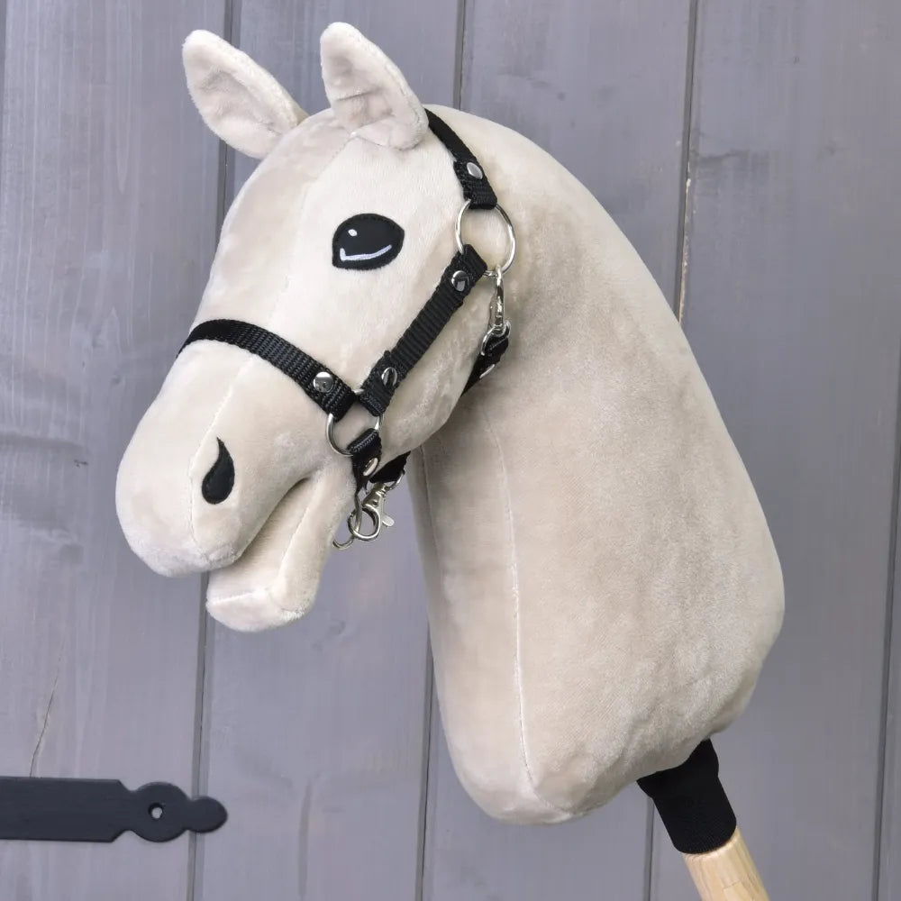 The Build your horse by related_to_12441055625556 features a light beige hobby horse head with a white yarn mane, black bridle and reins, attached to a wooden stick and set against a gray wooden background.