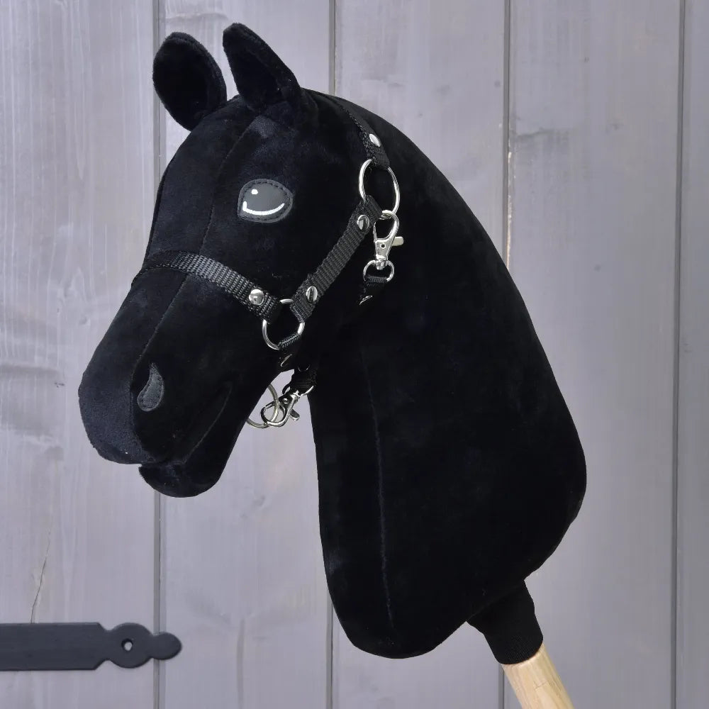 The Build your horse by related_to_12441055625556 features a black plush custom hobby horse head with a tricolor faux fur mane, bridle, and reins on a wooden stick, set before a gray wood panel—customize it just the way you like!.