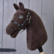 The "Build your horse" by related_to_12441055625556, featuring a dark brown body, white yarn mane, black bridle, and wooden stick, stands in front of a gray wooden wall.