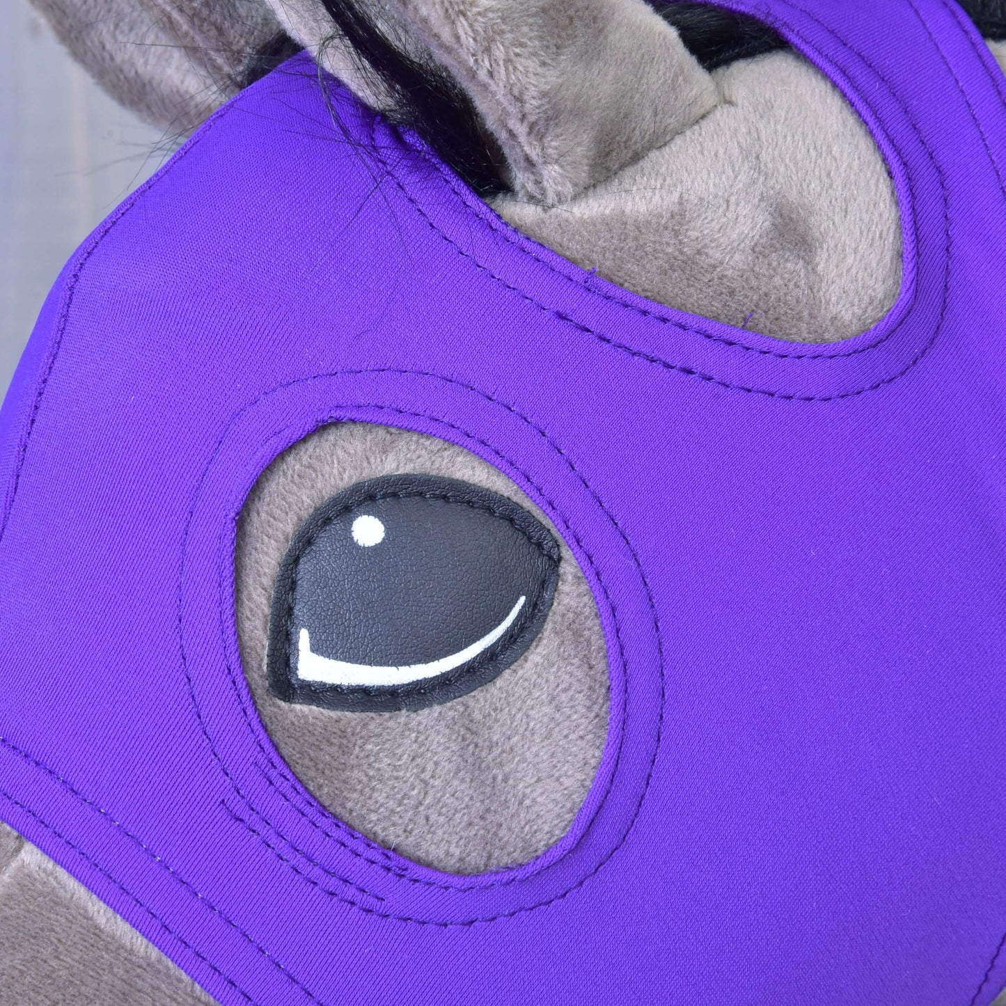 Detail sivého koňa s Maskou bez uší Indigo od Hobby Horse LarDen, jasne fialovou prateľnou maskou z PES s kresleným dizajnom oka a otvorom pre oko.