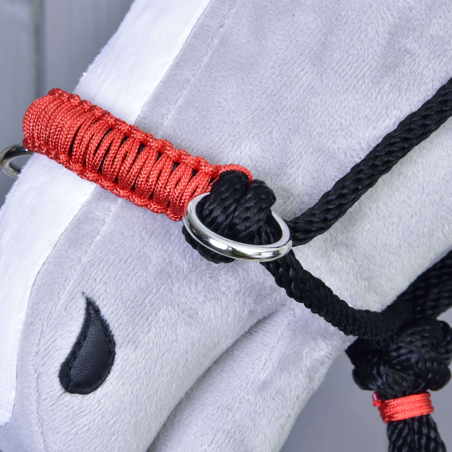Detail hlavy sivého plyšového koňa s Hobby Horse LarDen Parelka Jiskra v červenej a čiernej farbe s kovovým krúžkom a čiernou vyšívanou slzou pri oku. Ideálna ako jedinečný doplnok pre Hobby Horse.
