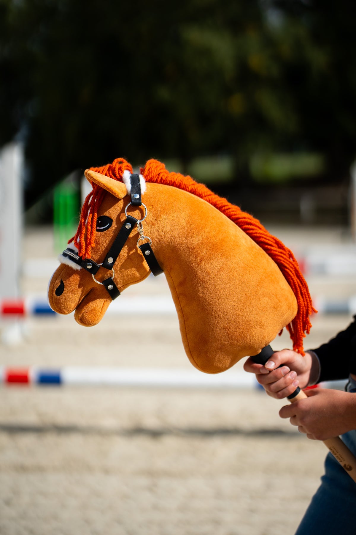 Hobby Horse Little Angel s čiernou ohlávkou držaný pri skokových tyčiach, s gaštanovou plyšovou hlavou a oranžovou priadzovou hrivou