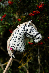 Hobby Horse Lord Valentine with Black Halter od Hobby Horse LarDen pred jarabinou s trsmi červených bobúľ, s bielou plyšovou hlavou s čiernymi leopardími škvrnami, krémovou priadzovou hrivou a čiernou ohlávkou so strieborným kovaním