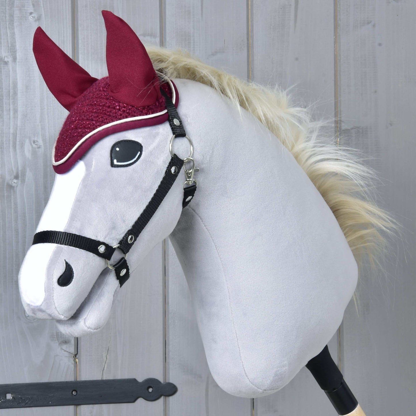 Čabraka Lux Maroon od Hobby Horse LarDen na plyšovom koni na tyči s bielou tvárou, čiernou uzdečkou, huňatou blond hrivou, gaštanovými látkovými ušami a ladiacou čabrakou na sivom drevenom pozadí.