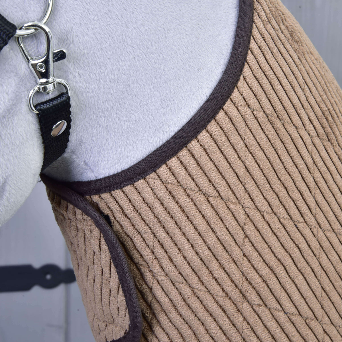Detail koňa v Set Manchester Le Chocolate od Hobby Horse LarDen s prešívaním v pieskovej farbe, hnedým lemom a čiernou ohlávkou so strieborným kovaním. Elegantný dizajn dopĺňa čiastočne viditeľná biela srsť koňa.