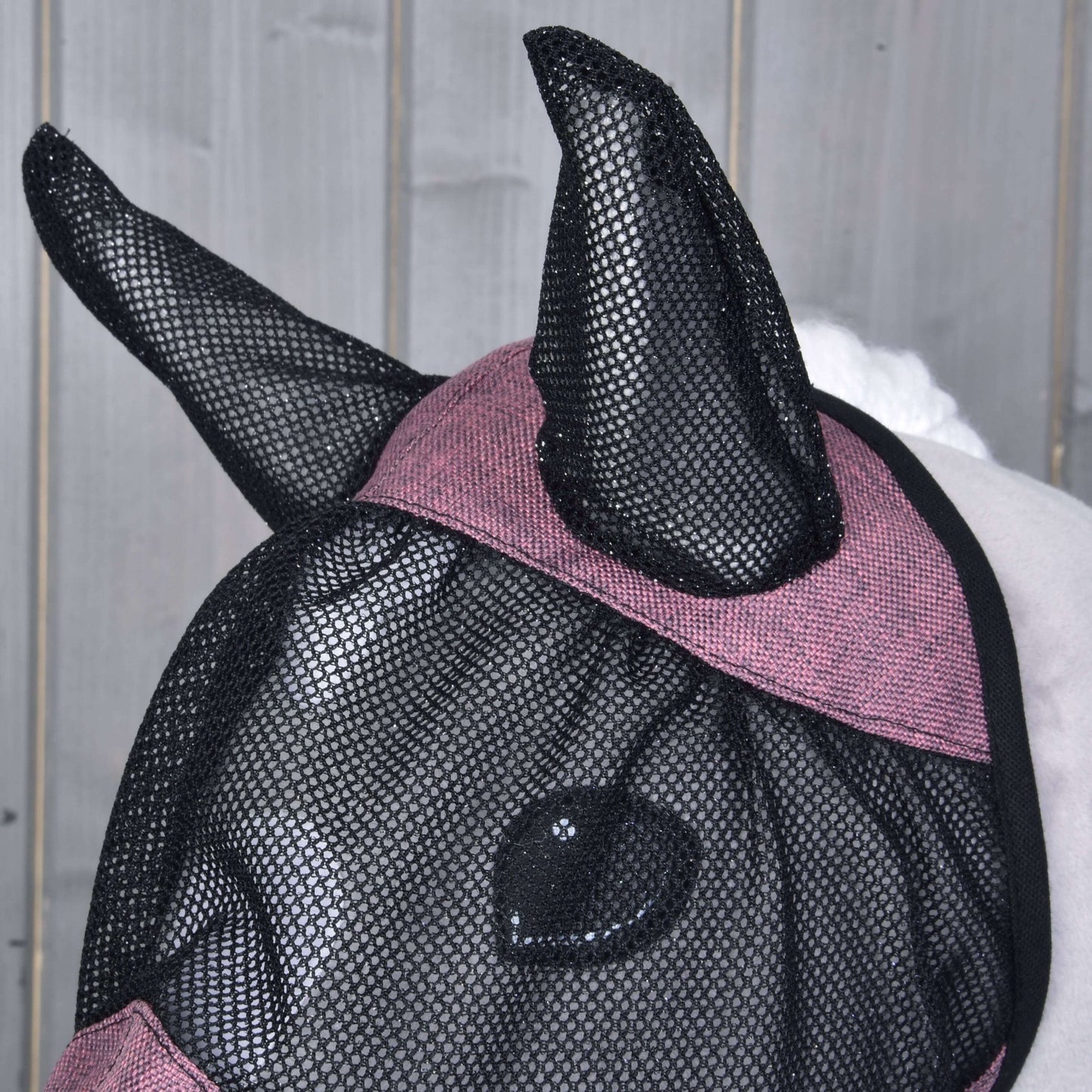Detail koňa v Maska proti hmyzu de Luxe Pink od Hobby Horse LarDen s vínovým lemovaním, zakrývajúcej uši, oči a časť tváre pre plnú ochranu, na svetlom drevenom pozadí.