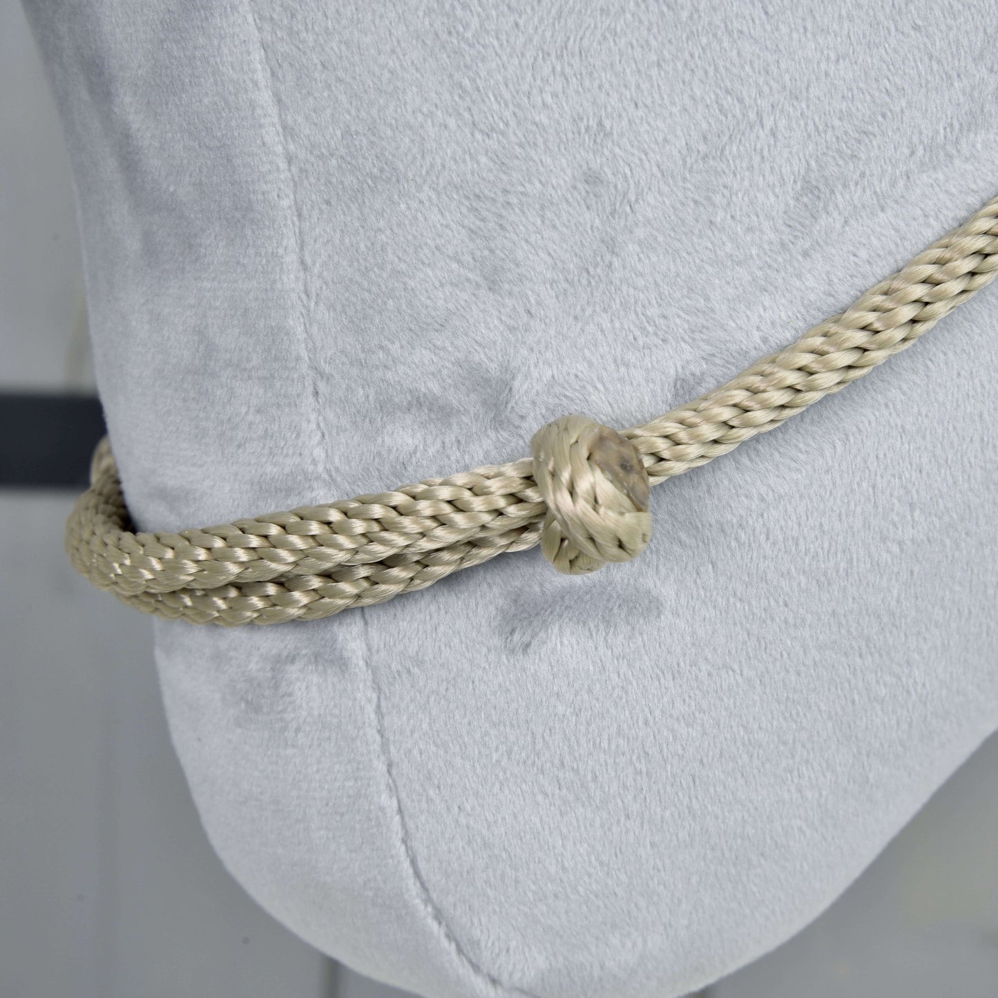 Detail nákrčníka Eleganza od Hobby Horse LarDen, silného svetlobéžového pleteného lana uviazaného do uzla okolo mäkkého bieleho vankúša, zvýrazňujúci výrazný kontrast textúry medzi cordeom a zamatovou látkou.
