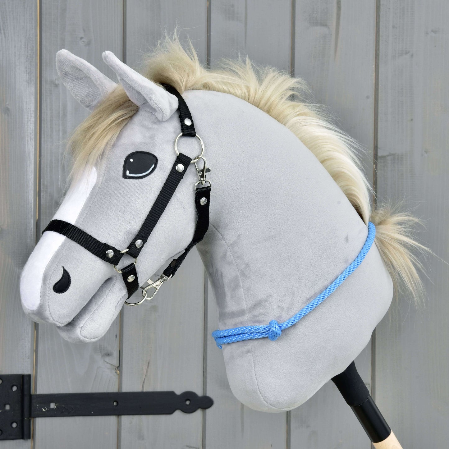 Nákrčník Sky od Hobby Horse LarDen je sivý plyšový Hobby Horse s bielou hrivou, čiernou uzdečkou a modrým lanom, navrhnutý na jazdenie s uzdečkou aj bez nej. Stojí pred dreveným pozadím a má priateľský výraz.