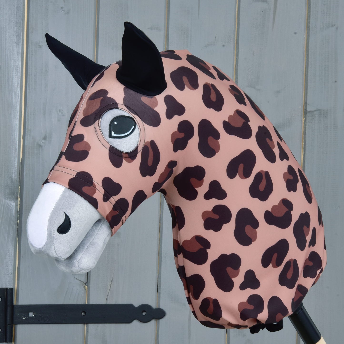 Hobby Horse ochranný oblek Glamour (Lycra) od Hobby Horse LarDen s růžovo-hnědým leopardím vzorem, černýma ušima a bílým čenichem, zobrazený na tyči před šedou dřevěnou stěnou.