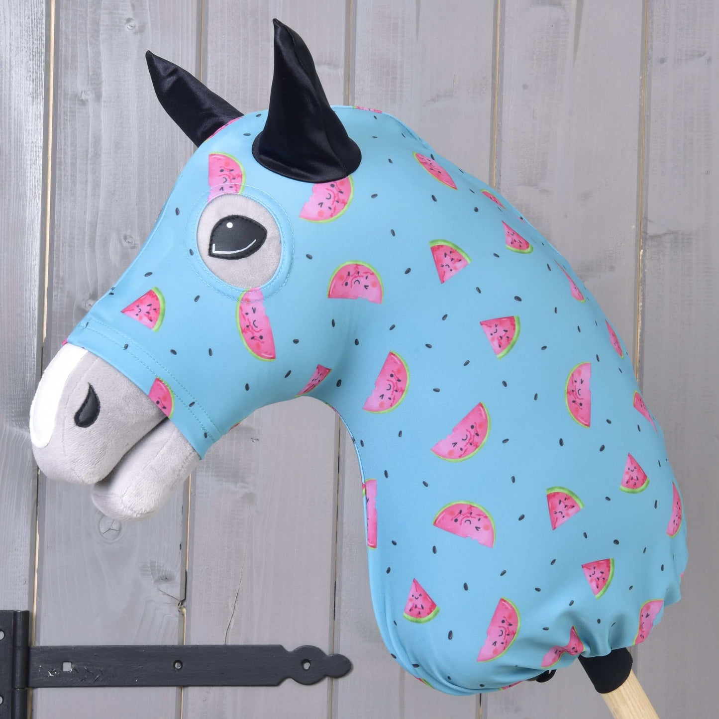 Hobby Horse ochranný oblek Melon (Lycra) od Hobby Horse LarDen má prateľný modrý poťah s ružovými plátkami melónu a čiernymi semienkami, navrhnutý pre plyšové hlavy Hobby Horse. Ideálny na ochranu, zobrazený na drevenej tyči pred svetlou stenou z drevených panelov.