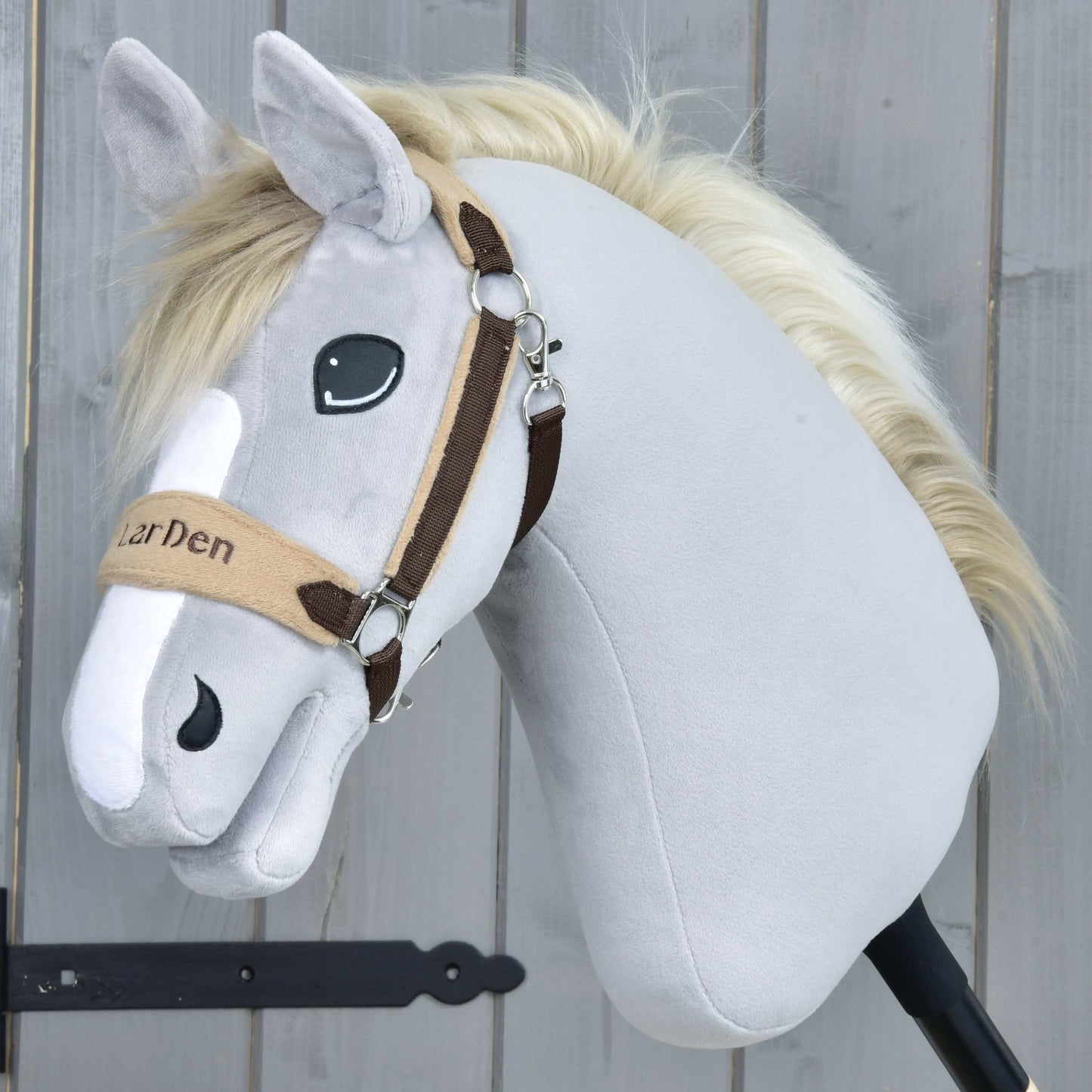 Hobby Horse LarDen Ohlávka s barančekom LarDen Brown so svetlosivým plyšom, krémovou hrivou, béžovohnedou ohlávkou s mäkkým fleecovým nánosníkom, vyšívanými očami a priateľským výrazom na drevenom pozadí.