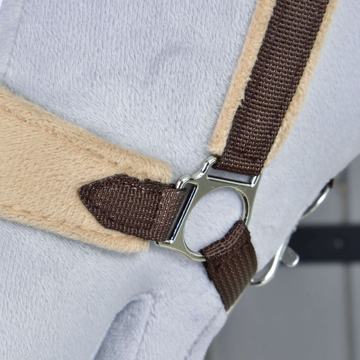 Detail ohlávky s barančekom LarDen Brown od Hobby Horse LarDen s hnedým popruhom, kovovým krúžkom a mäkkým barančekom na nánosníku na svetlosivom a béžovom povrchu, pripomínajúci časť plyšového doplnku pre Hobby Horse.