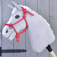 Šedý Hobby Horse LarDen s bílou hřívou, černýma očima a výrazně červenou parelkou Parelka červená bez omotu, nasazený na dřevěné tyči před šedou dřevěnou stěnou.