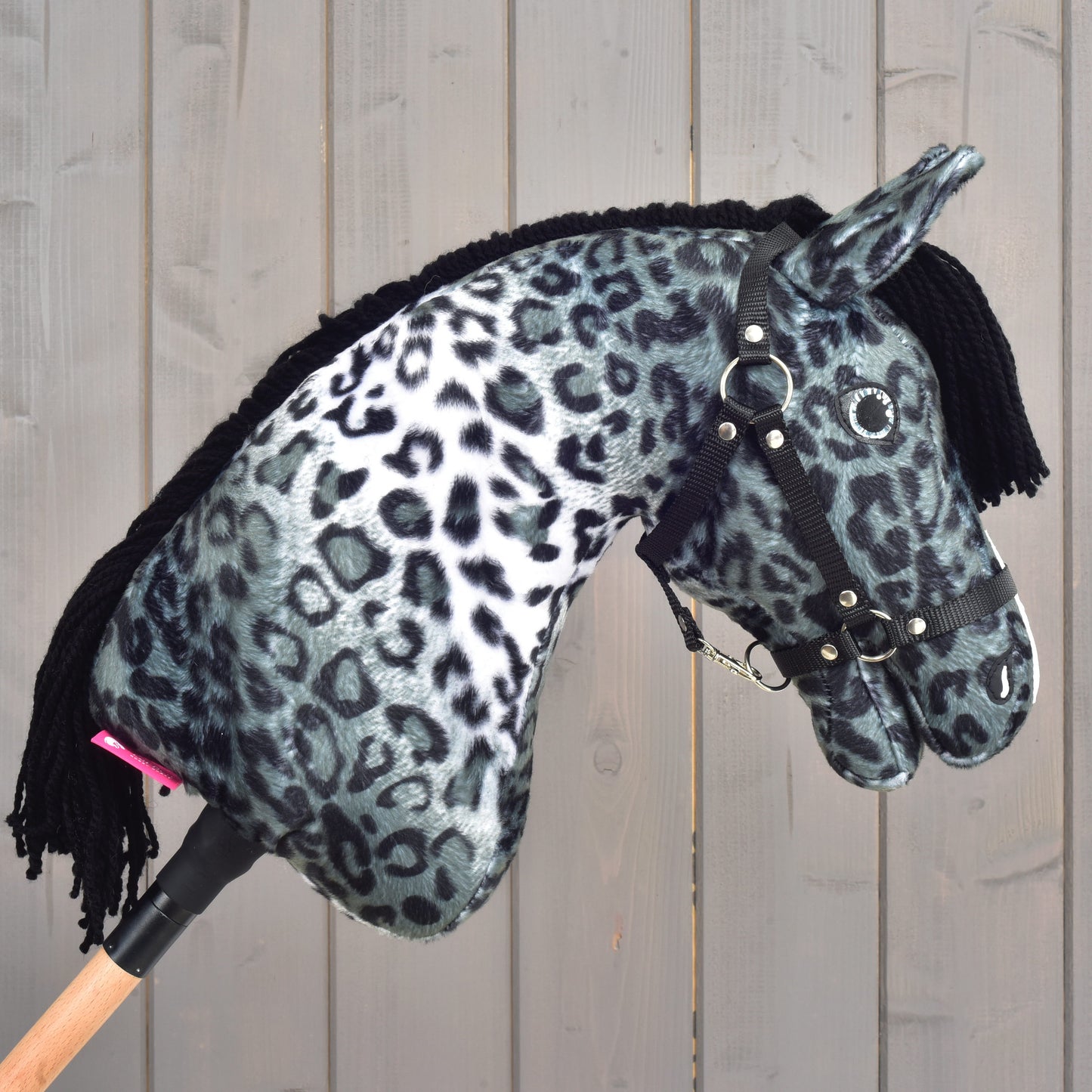 Hobby Horse Picasso s čiernou ohlávkou od Hobby Horse LarDen s mäkkým čiernobielym leopardím vzorom inšpirovaným škvrnitou srsťou appaloosy, doplnený čiernou priadzovou hrivou a čiernou ohlávkou, zobrazený na drevenom pozadí.
