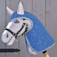 Pláštenka Dolly (softshell) od Hobby Horse LarDen so sivým Hobby Horse s modrou prikrývkou so vzorom kvapiek vody a uzdečkou na drevenej tyči – perfektná na hru za každého počasia na pozadí rustikálnych drevených dosiek.