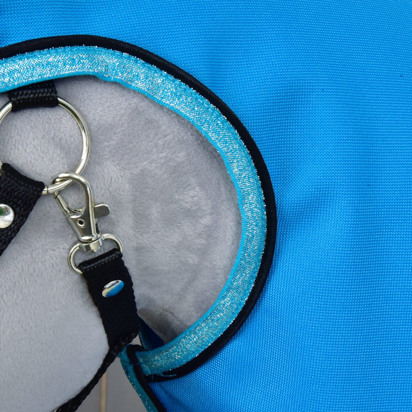 Detail pláštěnky Sky Blue od Hobby Horse LarDen s modrou látkou, šedým měkce podšitým vnitřkem, černým popruhem a kovovým D-kroužkem se zapínáním — ideální pro použití mazlíčkem za každého počasí.
