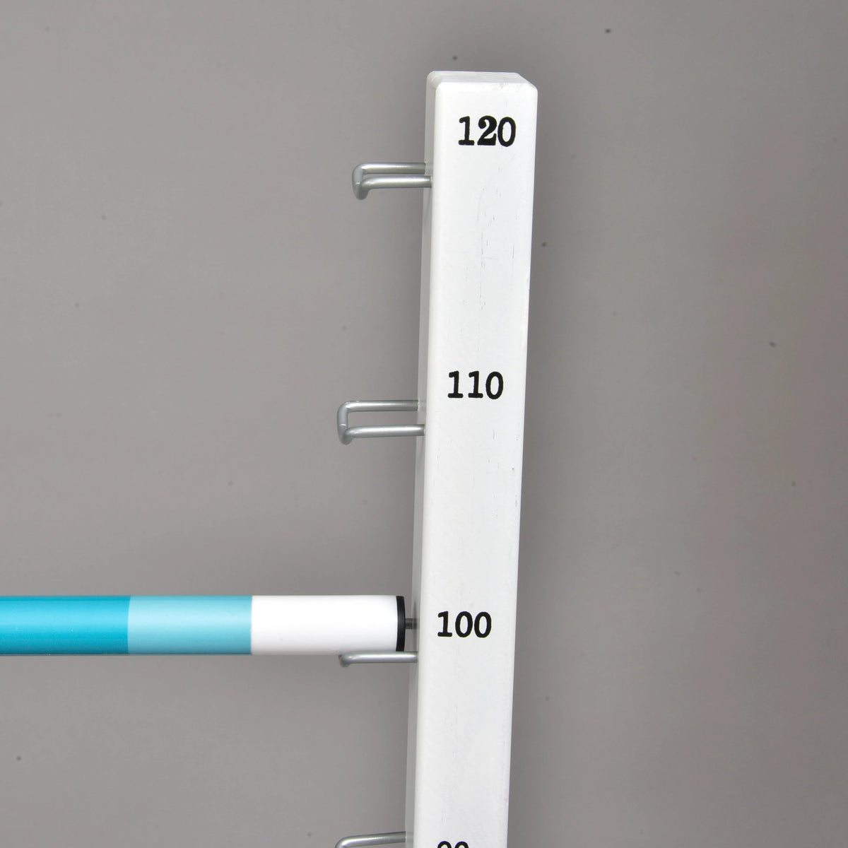 Prekážka kolmák 120 cm od Hobby Horse LarDen s bielym zvislým stojanom s háčikmi a výškovými značkami 100, 110 a 120, plus modrobiela vodorovná tyč nastavená na 100 — ideálna pre cavaletti alebo skákanie s Hobby Horse.