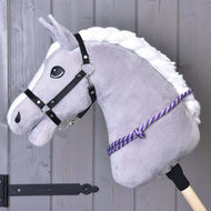 Nákrčník s fialovým prúžkom od Hobby Horse LarDen na sivom Hobby Horse s bielou hrivou, čiernou uzdečkou a ručne vyrábaným fialovým polypropylénovým cordeom na drevenej tyči, vyobrazený pred stenou z drevených dosiek.