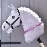 Nákrčník s ružovým prúžkom od Hobby Horse LarDen na sivej plyšovej konskej hlave s bielou hrivou, čiernou uzdečkou a ružovo-bielym nákrčníkom na drevenej tyči, ideálny pre nácvik jazdy bez uzdečky pred sivou drevenou stenou.