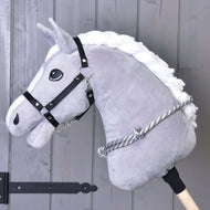 Nákrčník so strieborným prúžkom od Hobby Horse LarDen na plyšovom sivom Hobby Horse s bielou hrivou, čiernou uzdečkou a ručne vyrábaným sivo-bielym cordeom, zobrazený pred drevenými doskami s čiernym kovovým kovaním.