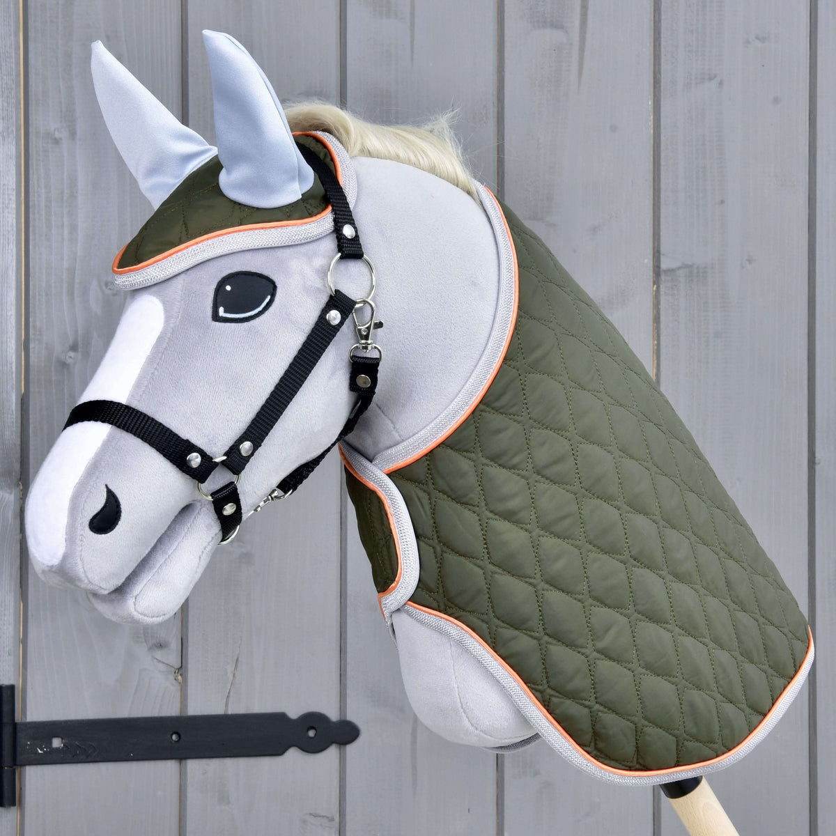 Set Moos od Hobby Horse LarDen so sivým Hobby Horse na drevenej tyči, čiernou uzdečkou, zelenou prešívanou dekou a svetlomodrou čabrakou na sivej drevenej stene.