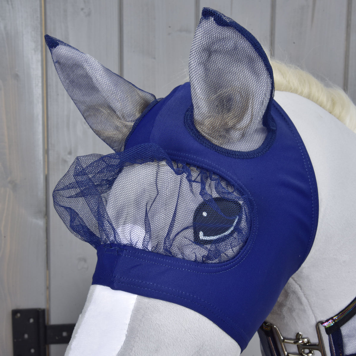 Biely kôň má na sebe Hobby Horse LarDen Set Fly Combo v námorníckej modrej so sieťovanými krytmi uší a očí. Ideálna pre štýl Hobby Horsing, táto maska chráni oči a uši tvojho koňa pred hmyzom.