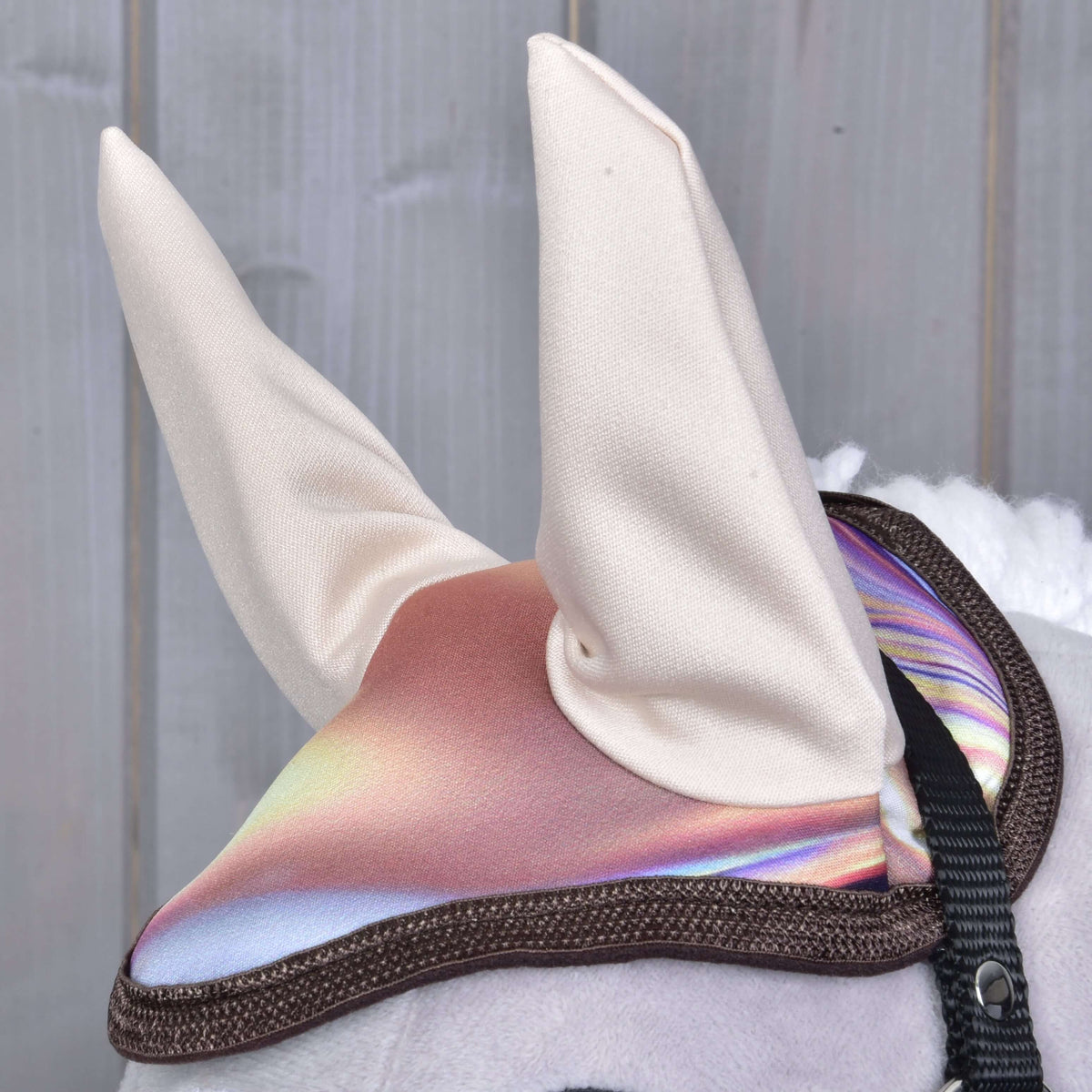 Detail Set Valery od Hobby Horse LarDen – hračka s lesklým, dúhovým ušným návlekom a dvoma bielymi vzpriamenými látkovými ušami. V pozadí rozmazané drevené panely.