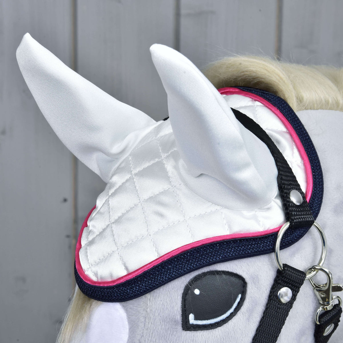 Detail Set Beautiful Star od Hobby Horse LarDen: sivý hračkársky kôň s bielou prešívanou čabrakou s ružovým lemom a tmavomodrým okrajom, čiernymi remienkami uzdečky a kreslenými očami, na pozadí svetlého dreveného obloženia — perfektná ochrana koňa.