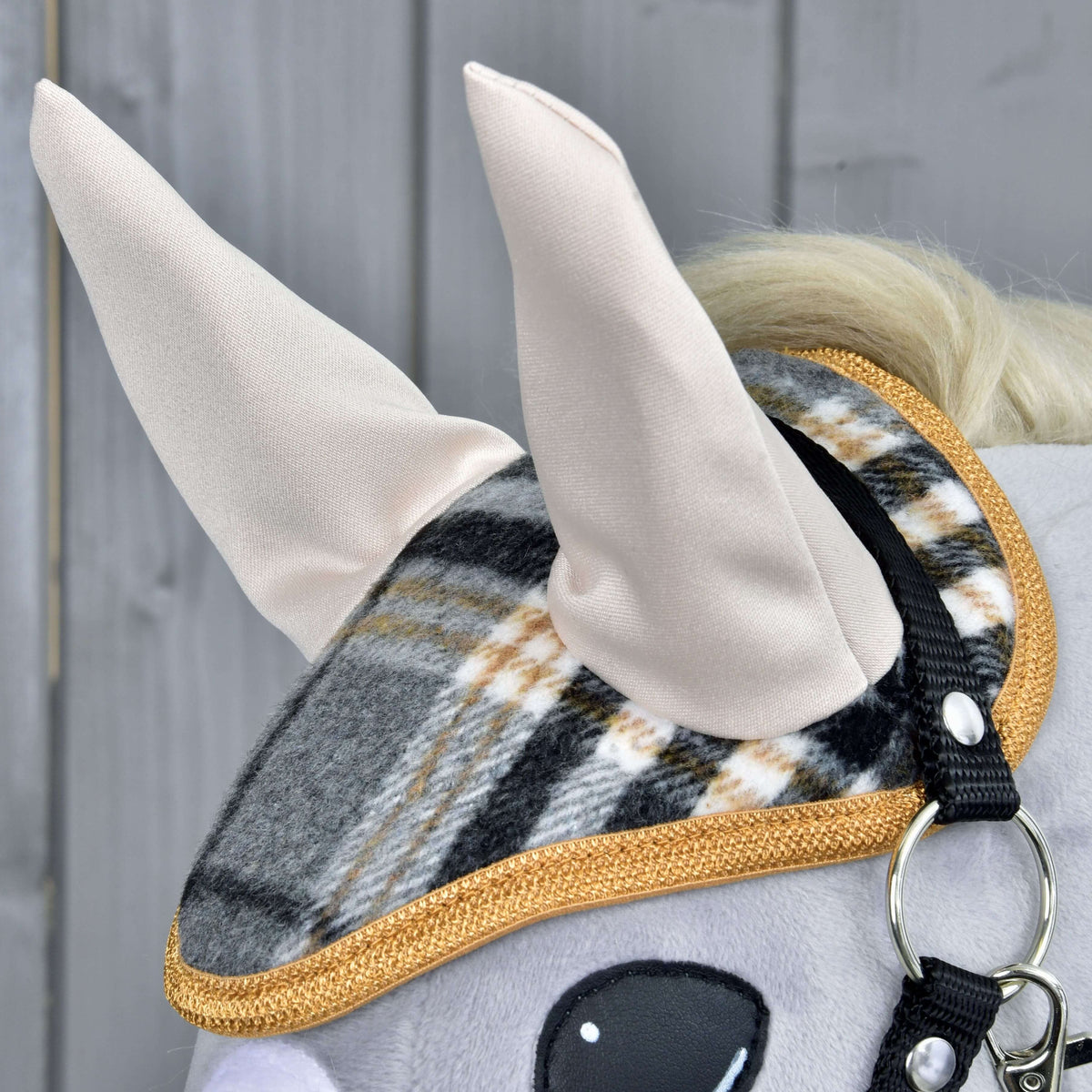 Set England Grey od Hobby Horse LarDen, detail plyšovej konskej hlavy s károvanou ohlávkou so zlatým lemovaním, čabrakou a mäkkými látkovými ušami na sivom drevenom pozadí – očarujúca konská dekorácia.