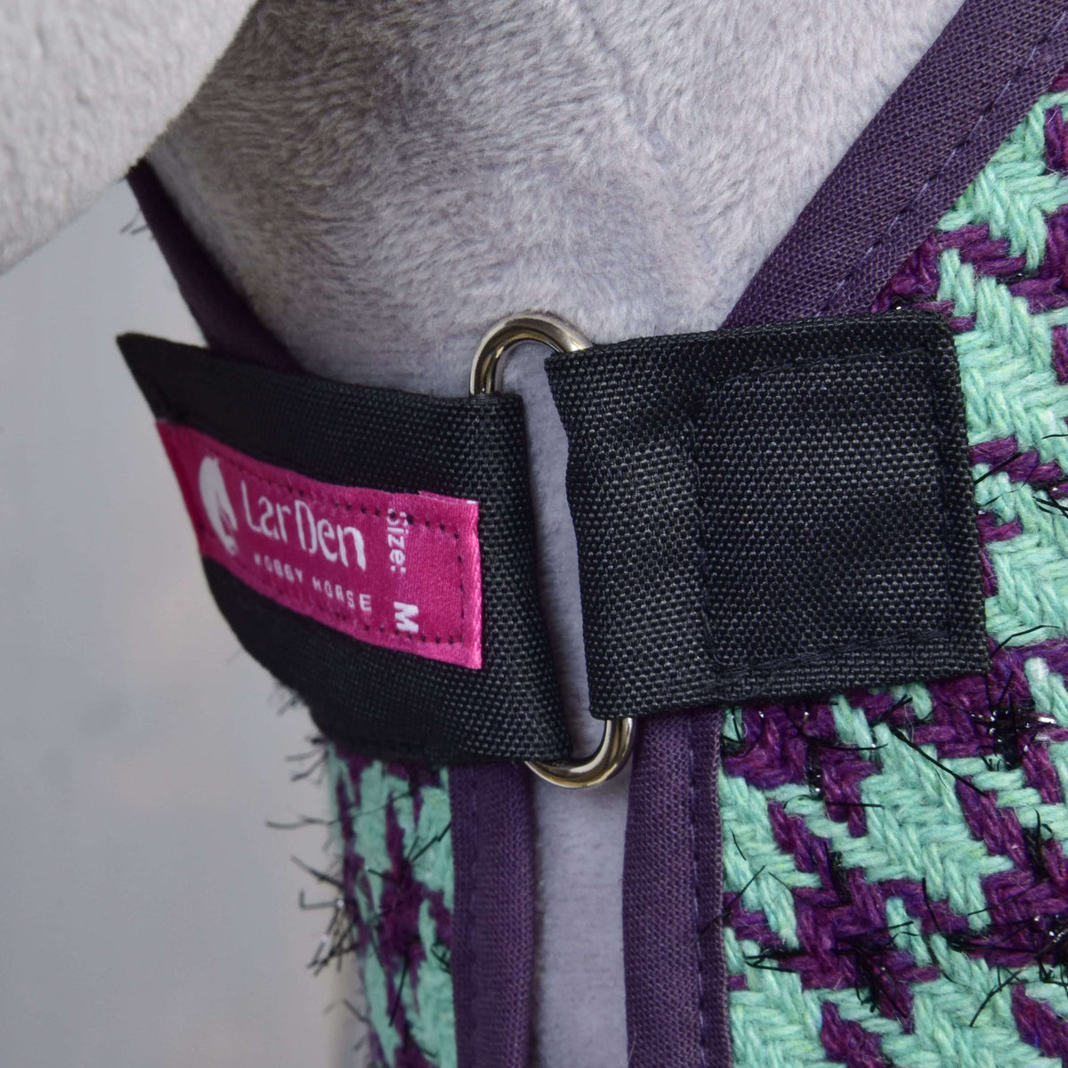 Detail postroja Set Harmony Green od Hobby Horse LarDen v purpurovo a zeleno tkanom prevedení, s čiernym remienkom s kovovým D-krúžkom a ružovým štítkom veľkosti M. Nasadené na svetlosivom Hobby Horse.