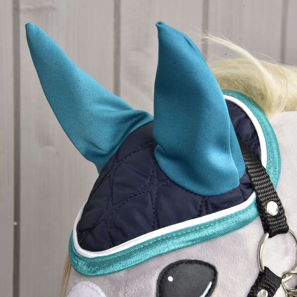 Detail Set Supreme Turquoise od Hobby Horse LarDen: plyšový koník má tmavomodrú prešívanú masku na oči s tyrkysovými špicatými krytmi uší a lemom – štýlovú súpravu čabraky – pre zábavu a ochranu, na pozadí svetlého dreva.