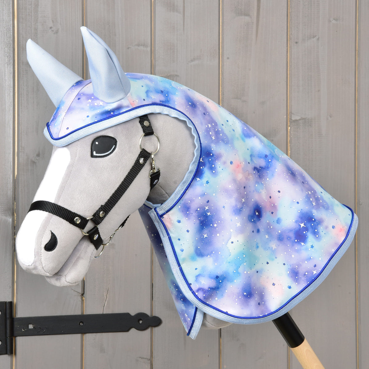 Hobby Horse LarDen Pláštenka Space s plyšovým Hobby Horse s čiernou uzdečkou a pastelovou hrivou a kapucňou s galaktickým vzorom v modrej, fialovej a ružovej farbe s bielym bodkovaním. Súčasťou je pláštenka na hru za každého počasia. Nasadené na drevenej tyči.