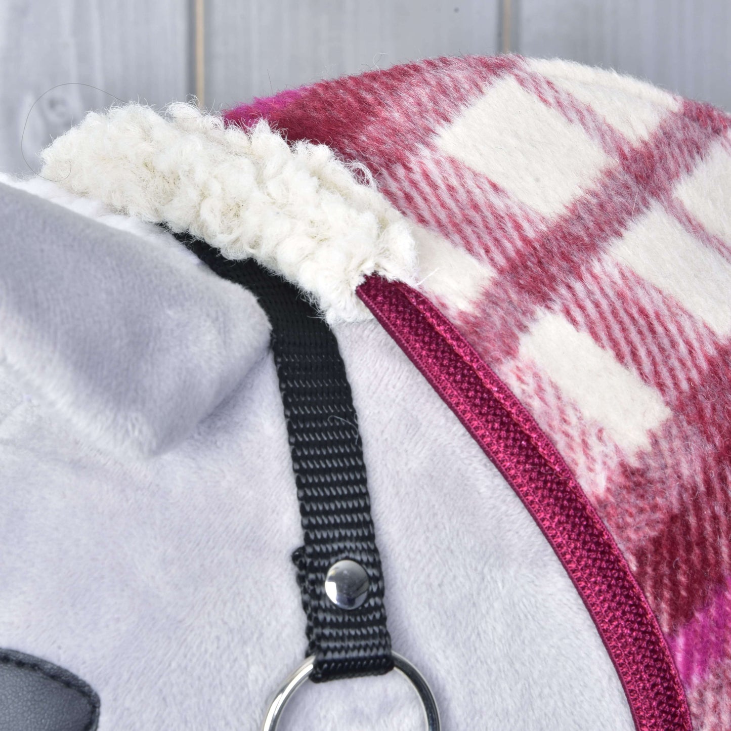 Deka stajňová LarDen od Hobby Horse LarDen na sivo-bielom plyšovom zvierati — červeno-biela károvaná fleecová deka s čiernym popruhom a kovovým krúžkom; plyšový materiál má viditeľné švy a mäkkú textúru.