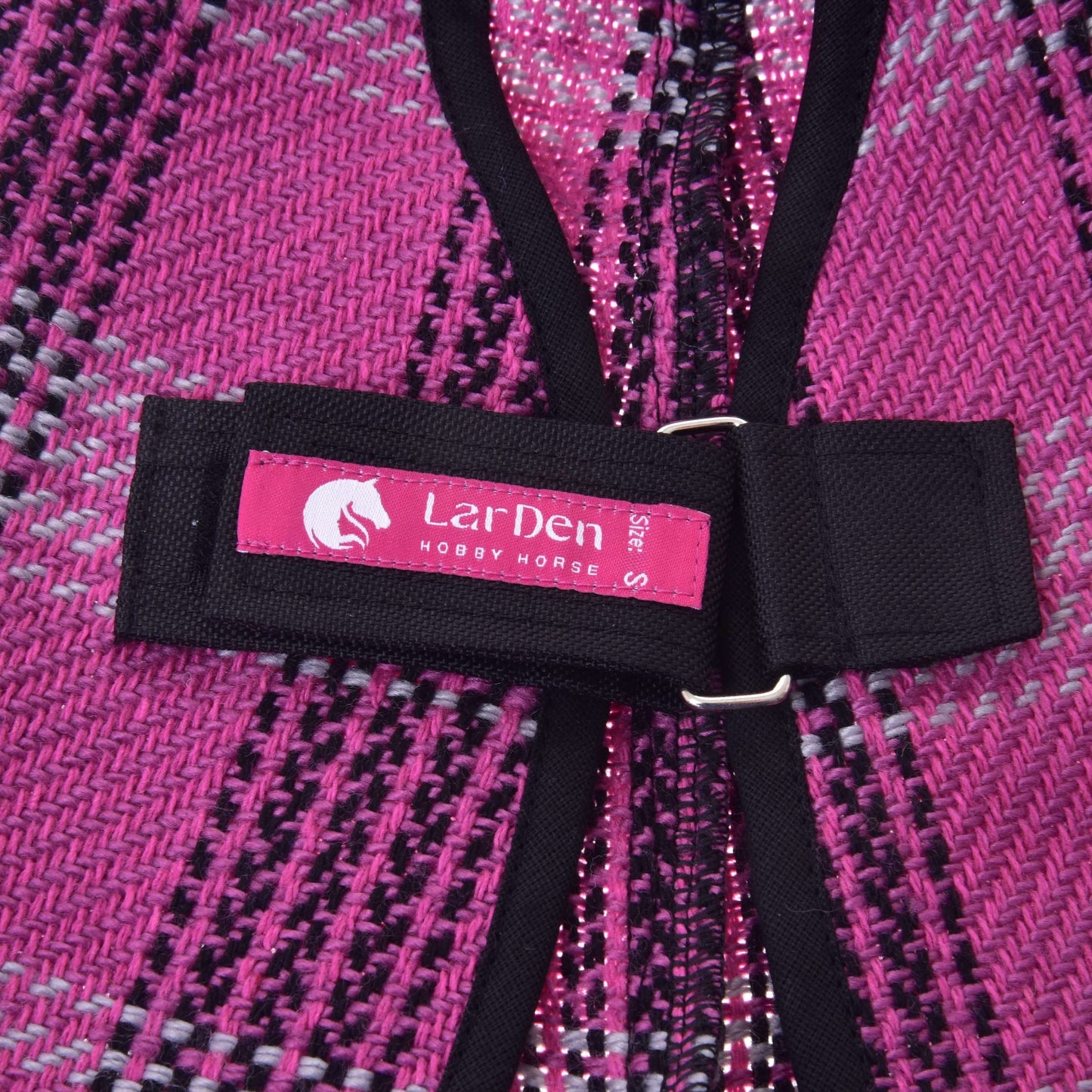 Detail deky Deka stajňová Pink od Hobby Horse LarDen s čiernym popruhom a ružovým štítkom s nápisom „LarDen HOBBY HORSE S size“ a logom konskej hlavy. Deka je tkaná v ružovej, čiernej a bielej farbe.