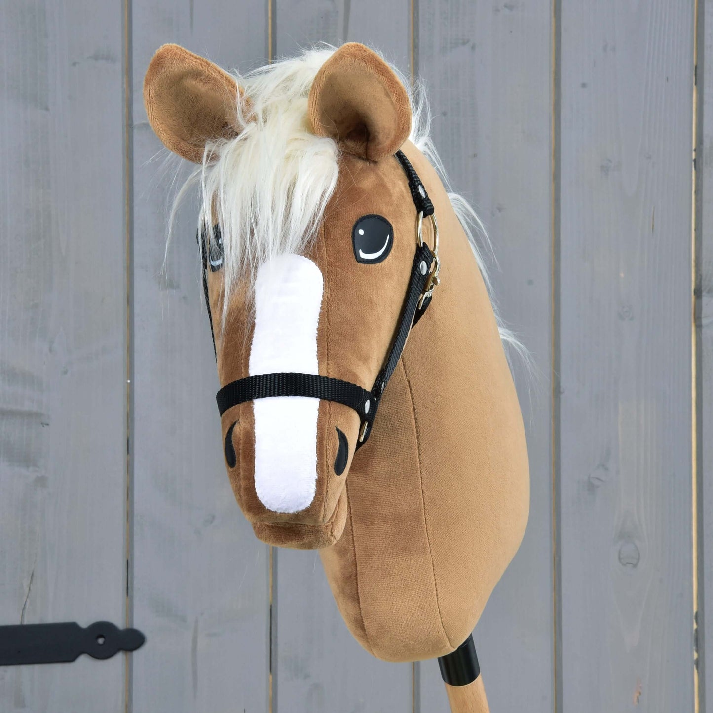 Hobby Horse Star s čiernou ohlávkou od Hobby Horse LarDen, s karamelovou srsťou, bielou lysinou, krémovou hrivou a čiernou ohlávkou, na sivom drevenom pozadí.