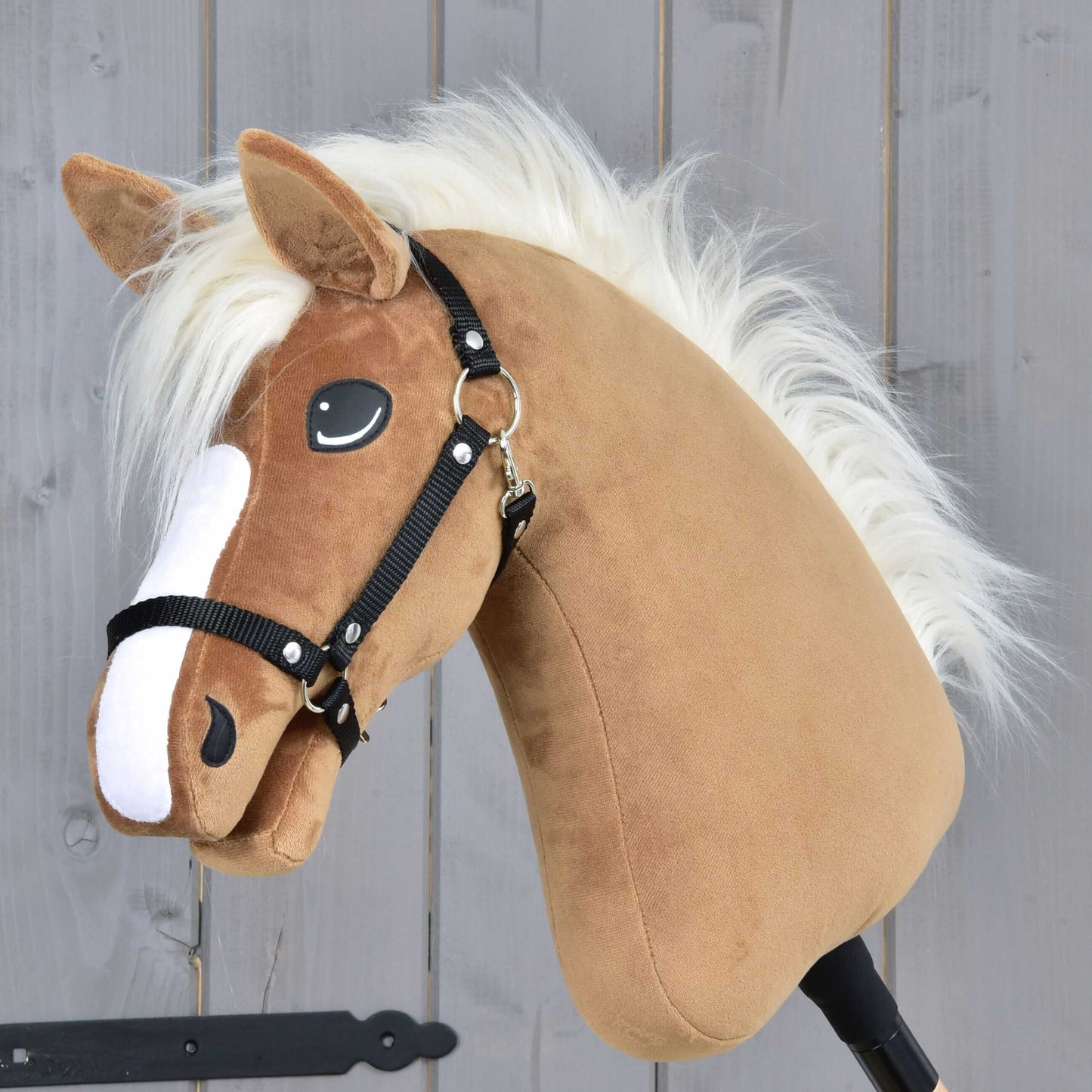 Hobby Horse Star s čiernou ohlávkou od Hobby Horse LarDen, s karamelovou srsťou, bielou hrivou a čiernou uzdečkou, na sivom drevenom pozadí.