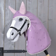 Hobby Horse LarDen „Pláštenka Sweetheart“ na plyšovom sivohlavom Hobby Horse s čiernou uzdečkou, ružovými ušami a levanduľovou pláštenkou so srdiečkovou potlačou – ideálna do každého počasia – nasadenom na drevenej tyči pred drevenou stenou.