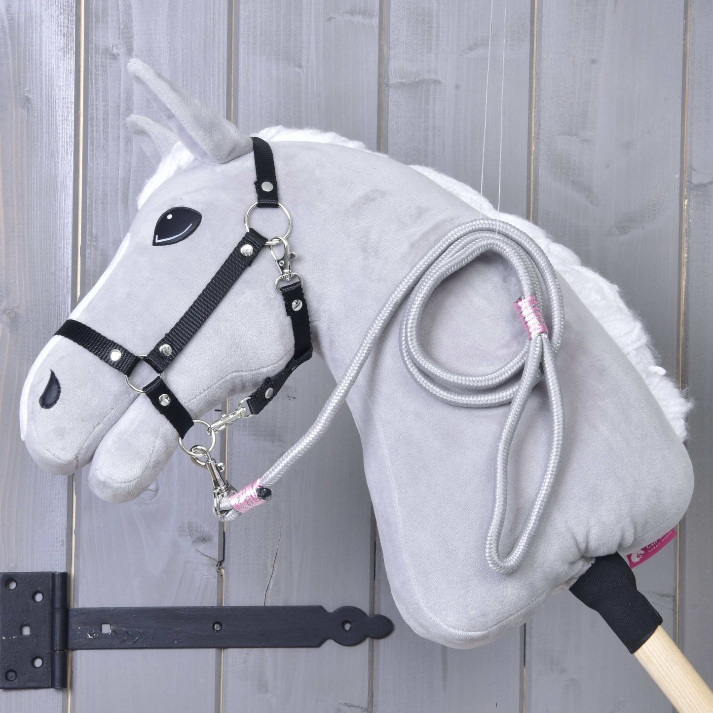 Hobby Horse - vodidlo Tizian od Hobby Horse LarDen v sivej farbe s čiernou uzdečkou, bielou hrivou a svetlou drevenou tyčou opreté o sivú stenu. Z krku visí stočené vodidlo, ideálne na hranie.