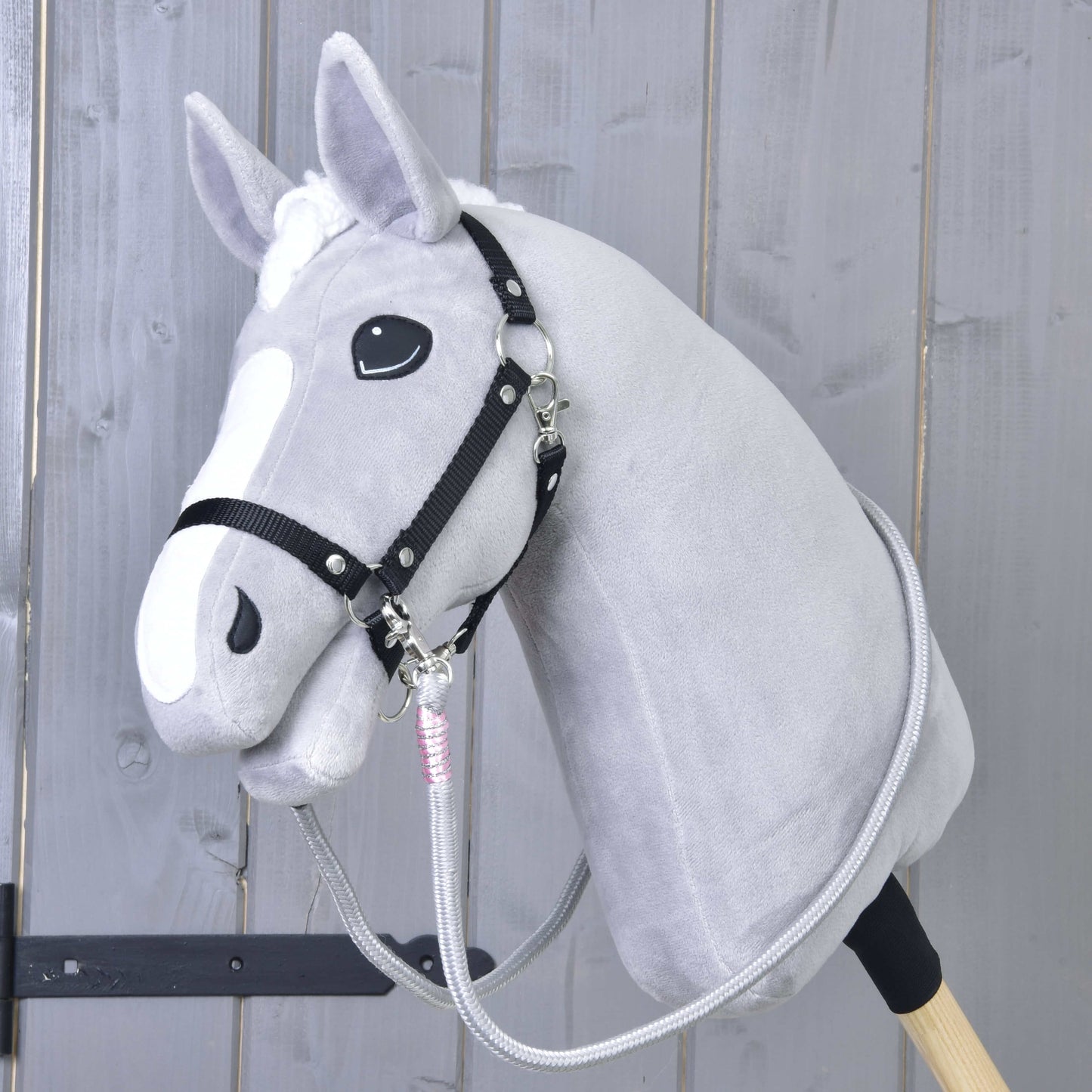 Hobby Horse LarDen Opraty Tizian na plyšovom sivom Hobby Horse s čiernou uzdečkou a ručne vyrábanými oprátami, na drevenej tyči pred svetlým dreveným panelovým pozadím.