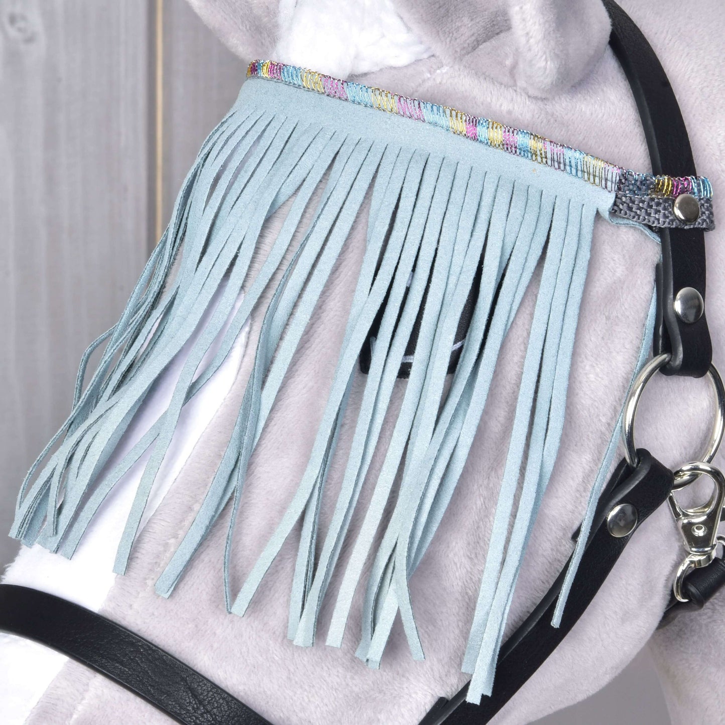 Detail světle šedého koně s černou ohlávkou od Hobby Horse LarDen se světle tyrkysovými třásněmi a barevným tkaným lemováním nad okem.