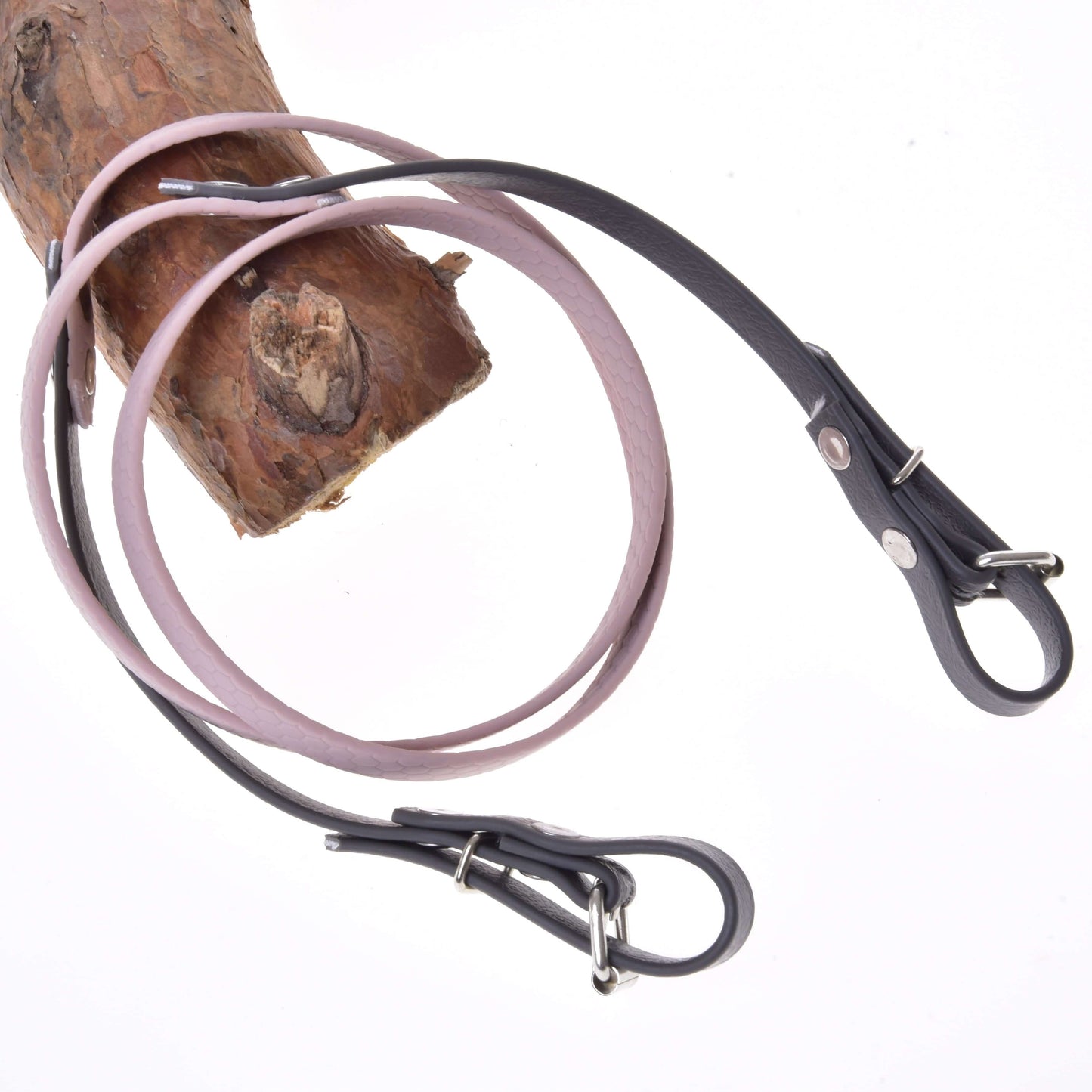 Opraty pogumované Dark Grey/pink od Hobby Horse LarDen dvakrát omotané okolo svetlohnedej drevenej vetvy, pripomínajúce kožené vodidlá pre psov, na bielom pozadí.