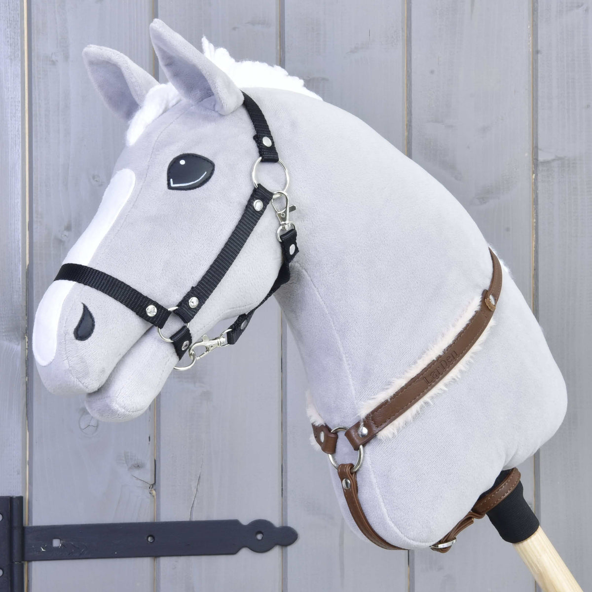 Poprsník s barančekom Walnut od Hobby Horse LarDen na plyšovom sivom Hobby Horse s bielou hrivou, čiernou uzdečkou, koženými oprátami a drevenou tyčou, na sivom drevenom pozadí.