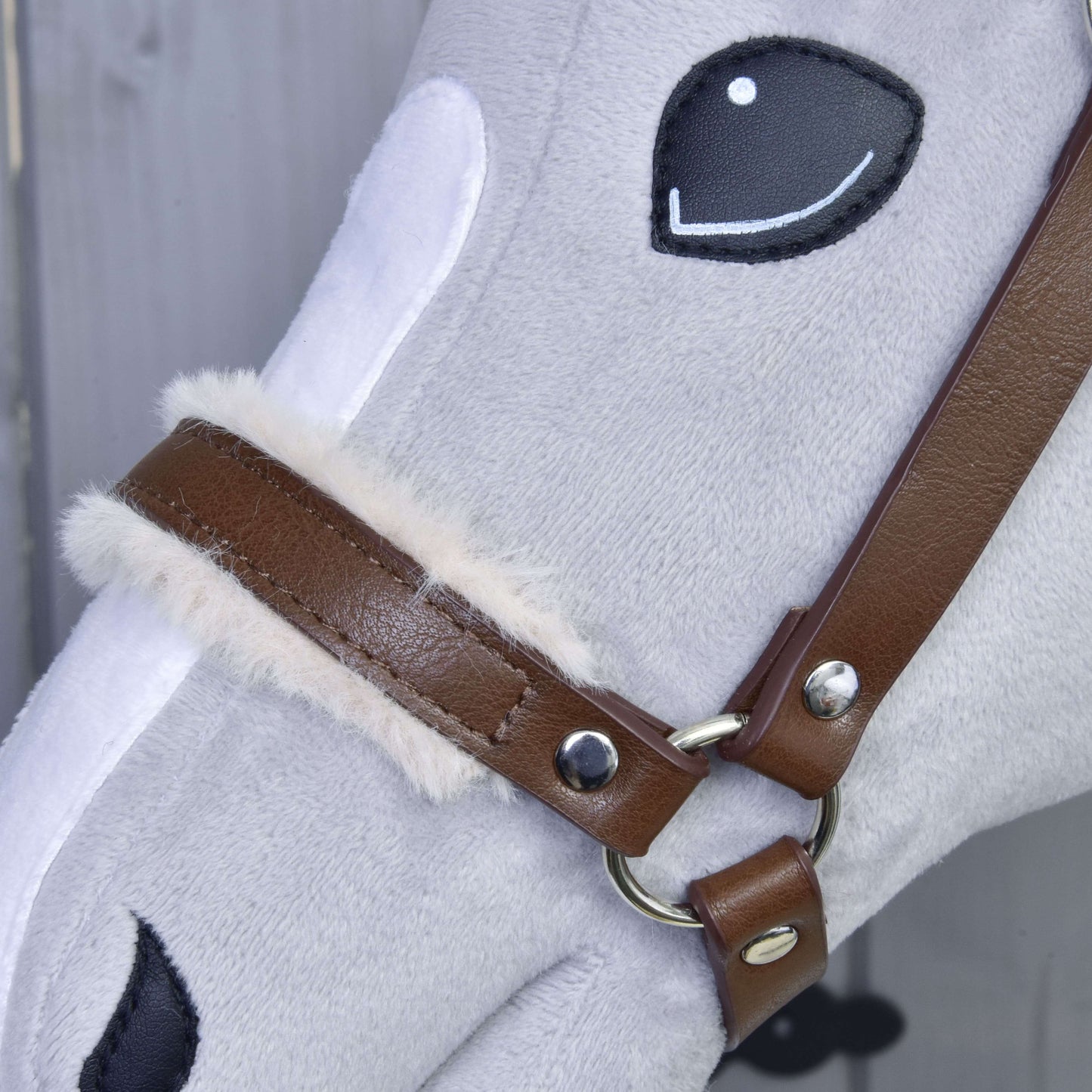 Detail tváre sivého plyšového koňa s vyšívanými čiernymi očami a nosom, ktorý má na sebe Ohlávku s barančekom z koženky Walnut od Hobby Horse LarDen s nadýchanou krémovou podšívkou pri pracke.