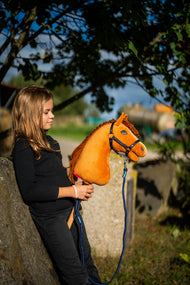 Dievča v čiernom tope sa opiera o kamenný blok pod stromom a drží Hobby Horse Wendy s čiernou ohlávkou od LarDen, žiarivogaštanová plyšová hlava a ryšavá priadzová hriva, s vodiacim lanom Blues rope stripe