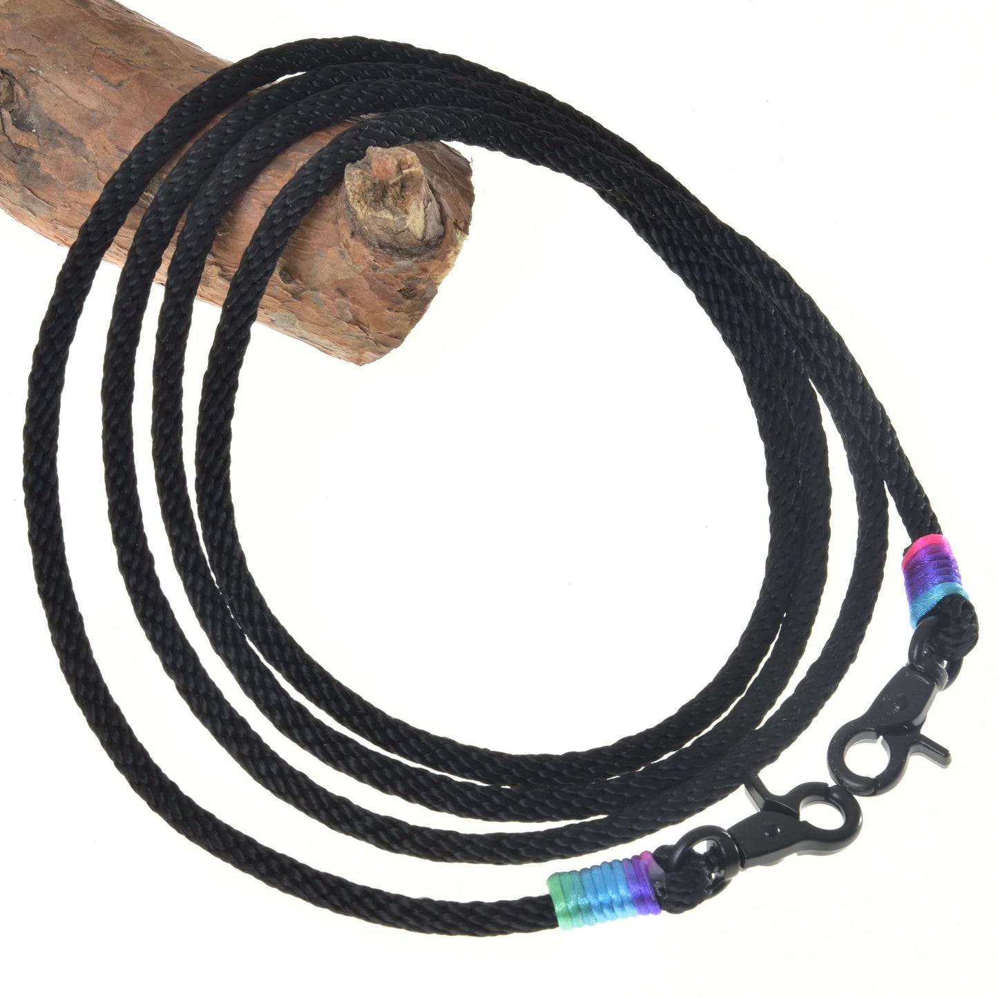 Westernové opraty Montana od Hobby Horse LarDen s čiernou pletenou šnúrou a karabínami na oboch koncoch, doplnené modrými, zelenými a ružovými pásikmi – ideálne na tréning alebo westernové jazdenie. Stočené do kruhu na bielom pozadí, s drevom vľavo hore.