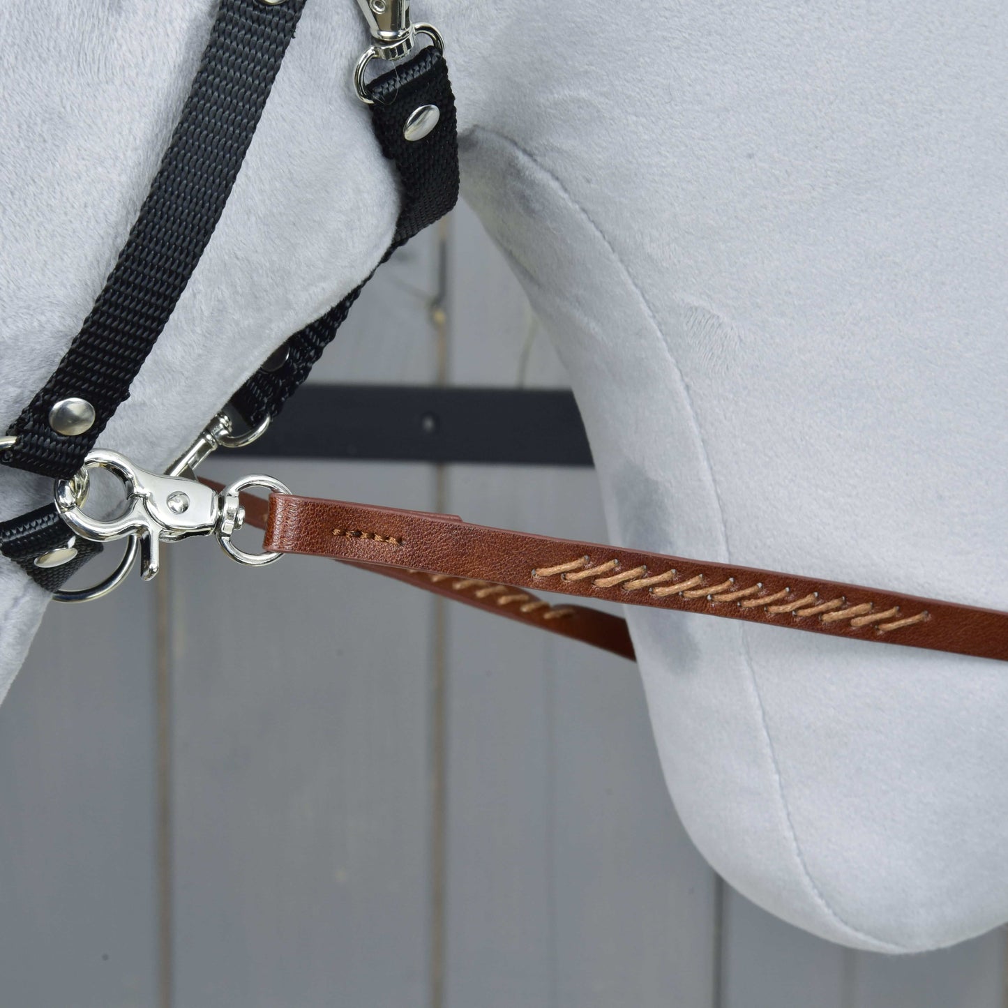 Westernové opraty Dark Brown od Hobby Horse LarDen, detail bielej konskej hlavy v uzdečke s opratami pripevnenými kovovým klipom, na pozadí svetlých drevených panelov.