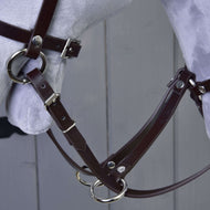 Detail Martingal hnedý od Hobby Horse LarDen s hnedou koženou uzdečkou s kovovými prackami a krúžkami na svetlosivej hlave modelu koňa na pozadí sivej drevenej steny.